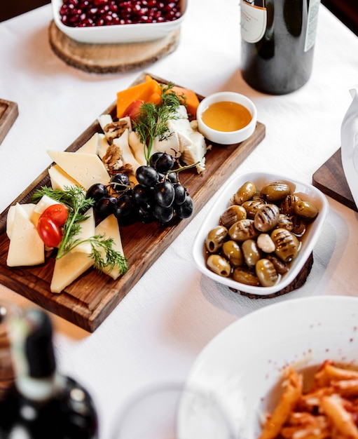 Vista laterale di vari tipi di formaggio con miele e uva sul piatto di legno con olive in salamoia