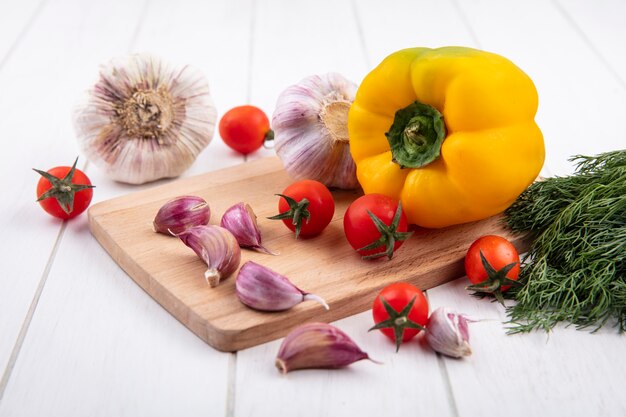 Vista laterale di verdure come aglio, pomodoro, pepe sul tagliere con aneto su legno