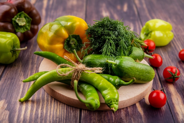 Vista laterale di verdure come aneto cetriolo pepe sul tagliere con pomodori su legno