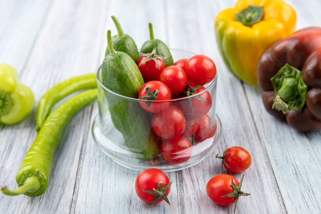 Vista laterale di verdure come pomodoro e cetriolo in una ciotola di vetro con pepe su legno