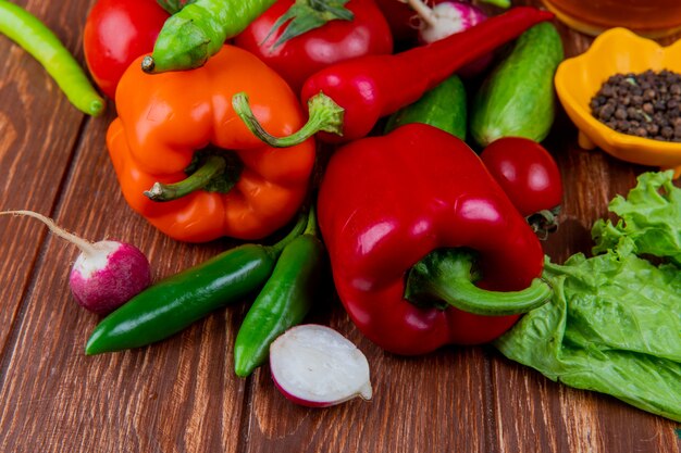 Vista laterale di verdure fresche colorate peperoni cetrioli pomodori maturi peperoncini verdi ravanello e grani di pepe neri su legno rustico