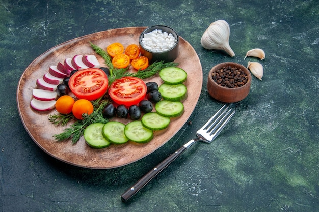 Vista laterale di verdure fresche tritate olive in un piatto marrone e forchetta pepe garlics su sfondo verde nero colori misti