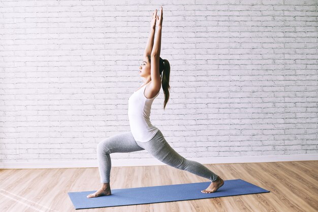 Vista laterale di yoga di pratica della ragazza adatta che fa una posa del guerriero sulla stuoia