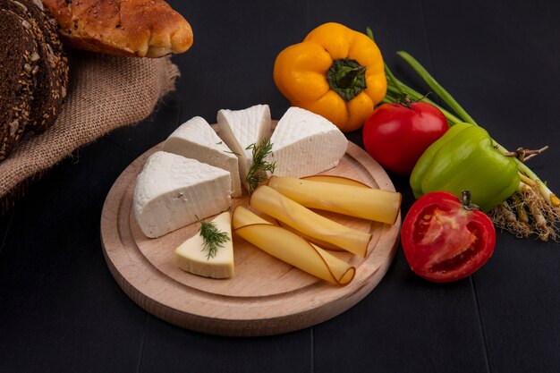 Vista laterale formaggio feta e pomodori peperoni e cipolle verdi su un supporto su uno sfondo nero