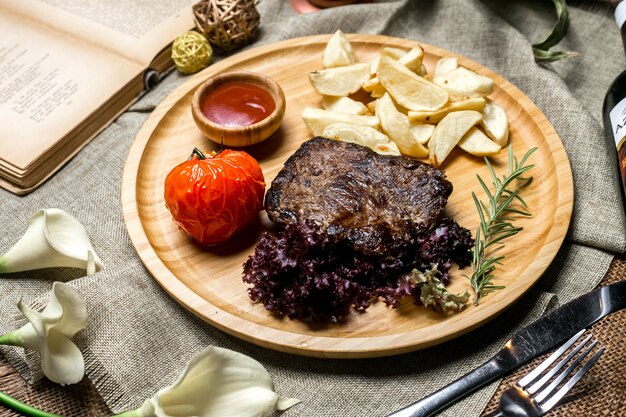 Vista laterale grigliata di carne rossa con patate in un ketchup di pomodoro rurale e rosmarino su una tavola