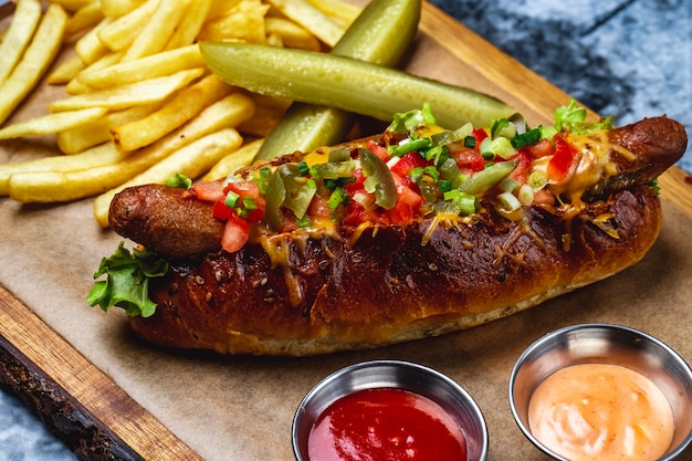 Vista laterale hot dog salsiccia alla griglia con pomodori verdi formaggio fuso jalapeno pepe nel panino hot dog con salsa di patatine fritte e cetriolo sottaceto su una tavola