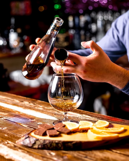 Vista laterale il barista versa da un bicchiere di whisky con cioccolato e fettine di arancia