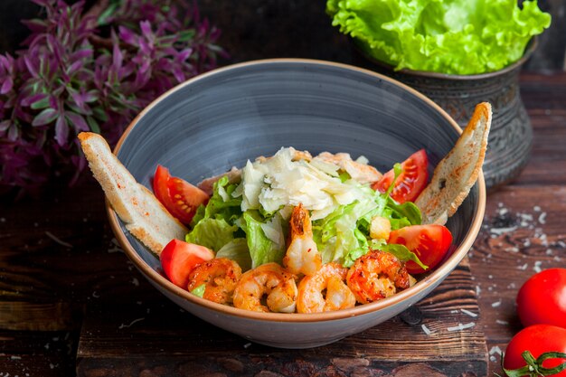 Vista laterale insalata caesar con petto di pollo e gamberi alla griglia, gamberi, pomodoro, insalata fresca in un piatto su un tavolo di legno scuro