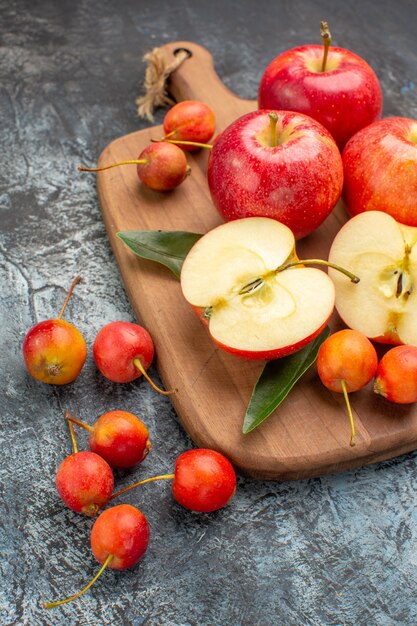 Vista laterale mele ciliege mele rosse con foglie sulla tavola di legno