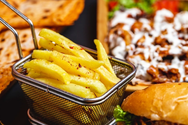 Vista laterale patatine fritte in acciaio inox mini cestino con sale e hamburger sul tavolo