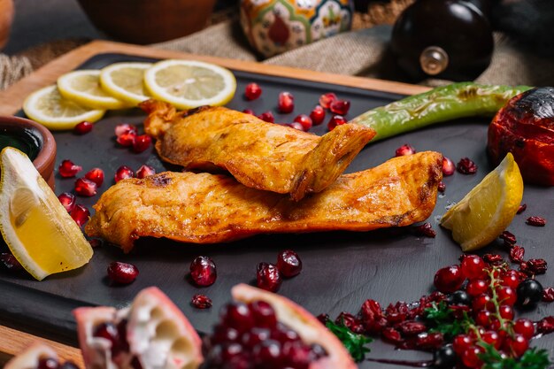 Vista laterale pesce grigliato con pomodoro e peperoncino grigliato con fette di limone melograno e salsa narsharab