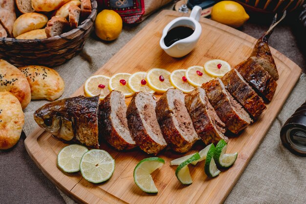 Vista laterale pesce ripieno con salsa di melograno lime limone e pane sul tavolo