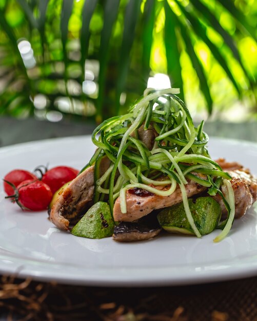 Vista laterale pollo alla griglia con zukini funghi cetriolo e pomodori su un piatto