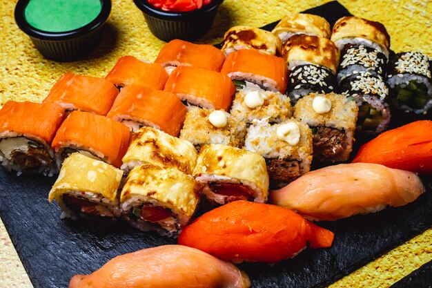 Vista laterale sushi set rotolo di uova con cetriolo e salmone philadelphia con crema di formaggio maki salmone nigiri wasabi e zenzero sul tavolo