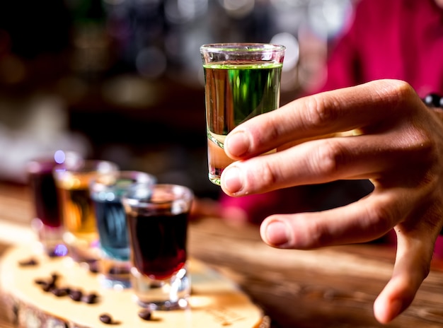 Vista laterale un uomo beve colpi colorati con chicchi di caffè su un pezzo di legno