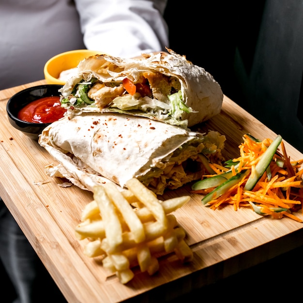 Vista laterale un uomo tiene un vassoio con doner di pollo nel pane pita con ketchup maionese patatine fritte e insalata di verdure sul tavolo