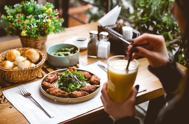 Vista laterale una donna beve il succo d'arancia con pollo fritto in pastella con erbe