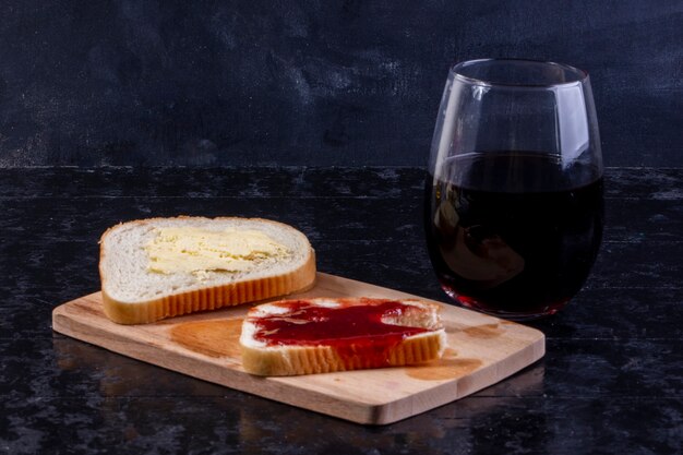 Vista laterale una fetta di pane e burro con una fetta di pane con marmellata a bordo con un bicchiere di succo