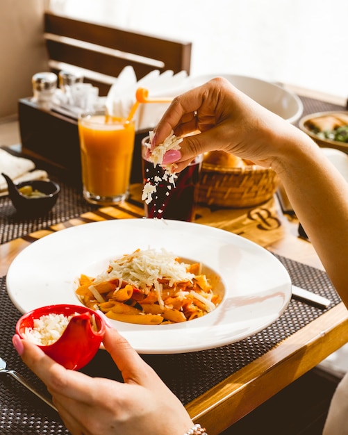 Vista laterale una ragazza spruzza formaggio grattugiato pasta