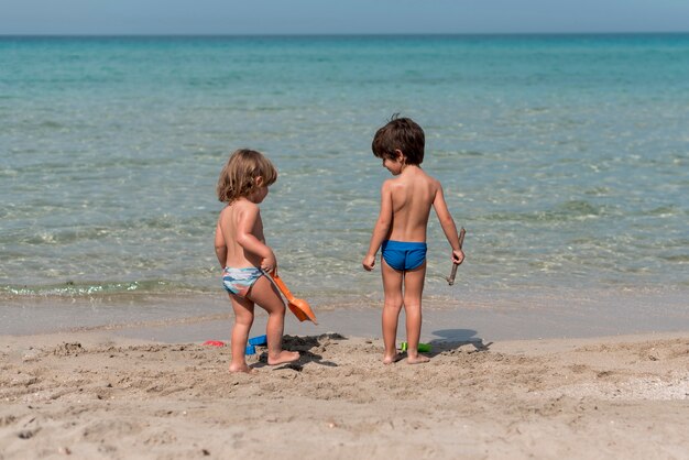 Vista lunga dei bambini che stanno alla spiaggia con i giocattoli