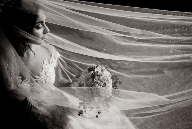 Vista monocromatica di una bella sposa tenera con bouquet da sposa e velo lungo con gli occhi chiusi