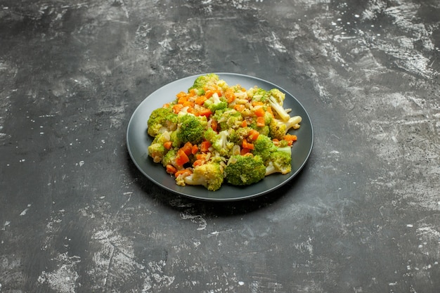 Vista orizzontale del pasto sano con broccoli e carote su un piatto nero sul tavolo grigio