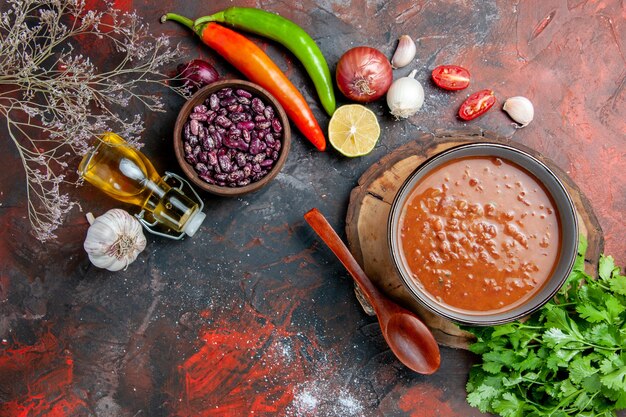 Vista orizzontale della classica zuppa di pomodoro con cibi e fagioli bottiglia di olio e un mazzo di limone verde pomodoro sul tavolo di colori misti