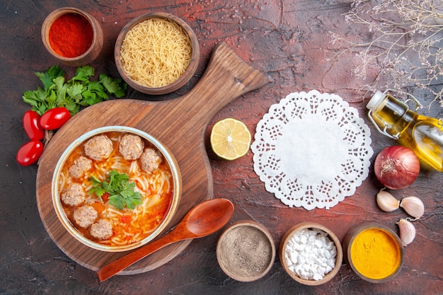 Vista orizzontale della zuppa di polpette di pomodoro con noodles in una ciotola marrone e diverse spezie bottiglia di olio cipolla aglio e tovagliolo su sfondo scuro