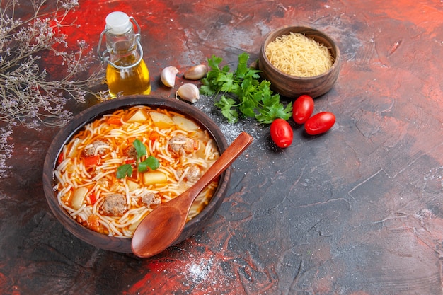 Vista orizzontale di deliziosa zuppa di noodle con pollo e pasta cruda in una piccola ciotola marrone e cucchiaio di pomodori e verdure all'aglio sullo sfondo scuro