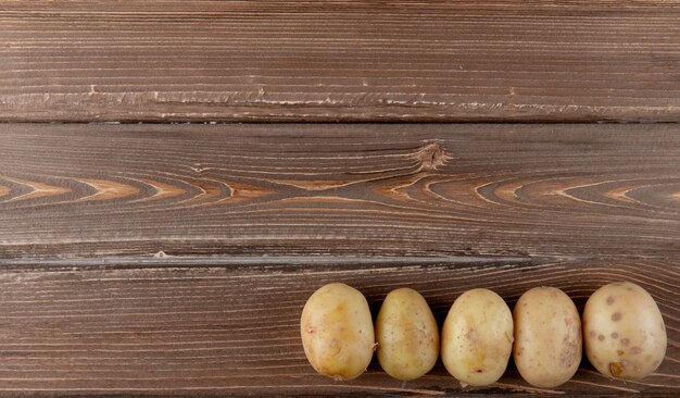 Vista orizzontale di intere patate dalla parte di destra e fondo di legno con lo spazio della copia