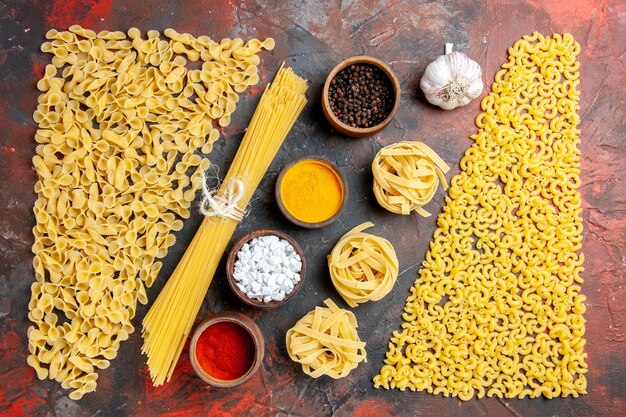 Vista orizzontale di pasta cruda in varie forme e diverse spezie sulla tavola nera