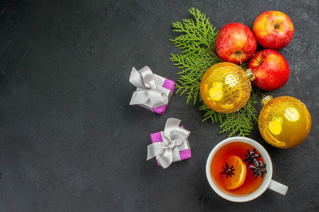 Vista orizzontale di regali e mele fresche biologiche naturali e accessori decorativi una tazza di tè su sfondo nero