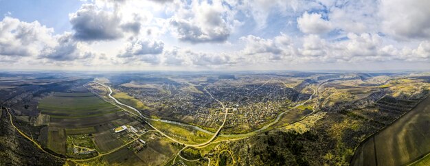 Vista panoramica aerea drone di un villaggio situato vicino a un fiume e colline, campi, godrays, nuvole in Moldova