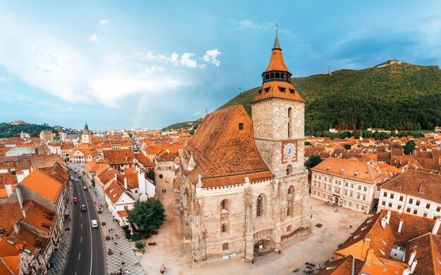 Vista panoramica del drone aereo della Chiesa Nera nel vecchio centro di Brasov, Romania Vecchi edifici residenziali intorno ad essa strade strette con auto in movimento colline con verde