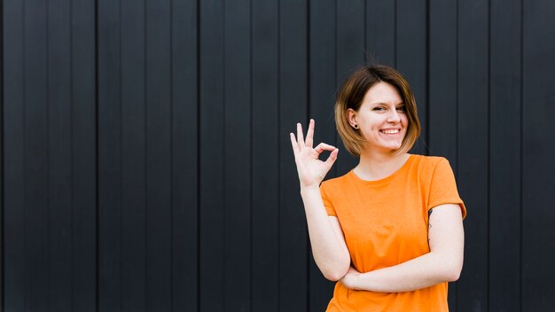 Vista panoramica di un ritratto sorridente di una giovane donna che mostra segno giusto