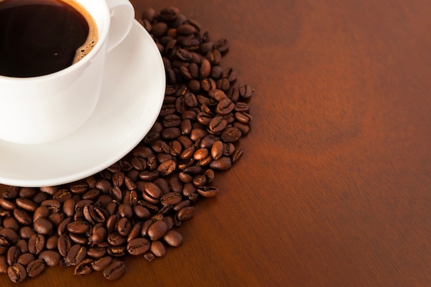 Vista parziale della tazza di caffè e dei fagioli sul tavolo di legno