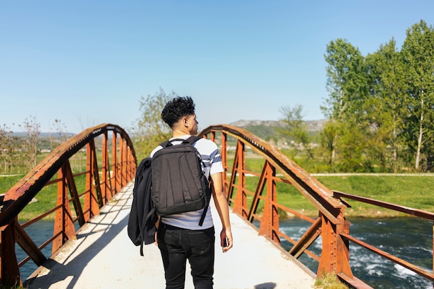 Vista posteriore del giovane che cammina sul ponte sul bellissimo fiume