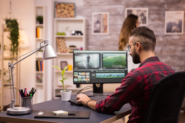 Vista posteriore del regista creativo che lavora su un film sul laptop. Fidanzata in sottofondo.