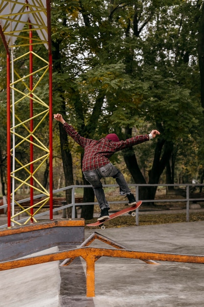 Vista posteriore dell'uomo che fa i trucchi con lo skateboard all'aperto nel parco