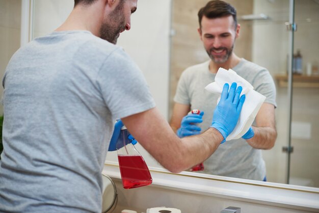 Vista posteriore dell'uomo che pulisce lo specchio in bagno