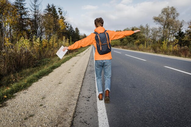 Vista posteriore dell'uomo che tiene la mappa e cammina lungo la strada