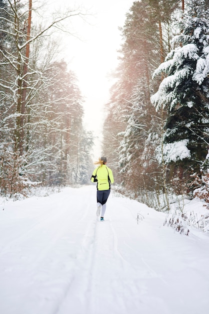 Vista posteriore della donna che corre nella foresta invernale