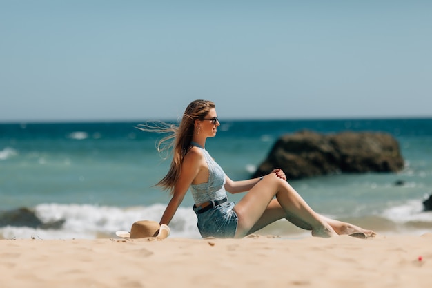 Vista posteriore della donna di vacanze al mare che gode del sole di estate che si siede nella sabbia che sembra felice allo spazio della copia. Bellissima modella giovane