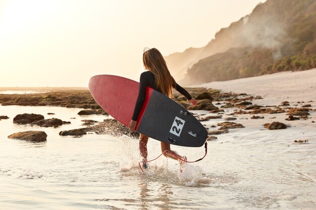 Vista posteriore della donna in esecuzione entra in acqua calda dell'oceano per le attività di surf