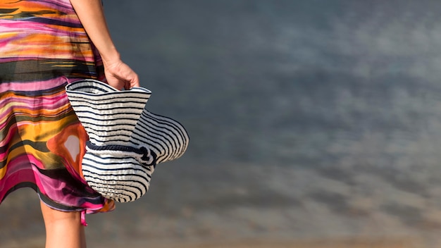 Vista posteriore della donna in spiaggia tenendo il cappello