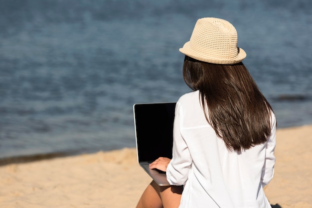 Vista posteriore della donna sulla spiaggia con il computer portatile
