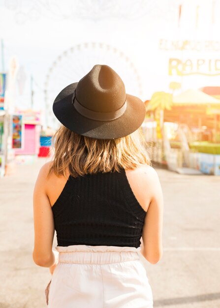 Vista posteriore della giovane donna che indossa cappello nero in piedi al luna park