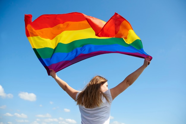 Vista posteriore della giovane donna che sventola bandiera arcobaleno