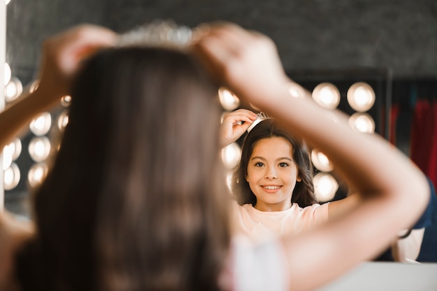 Vista posteriore della ragazza che indossa la corona sulla sua testa guardarsi allo specchio