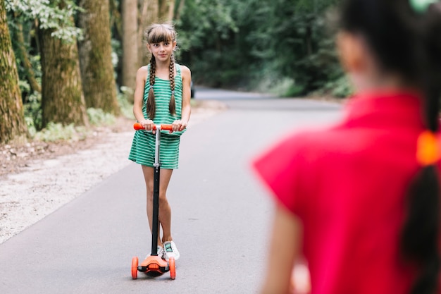 Vista posteriore della ragazza guardando il suo amico in piedi su scooter push